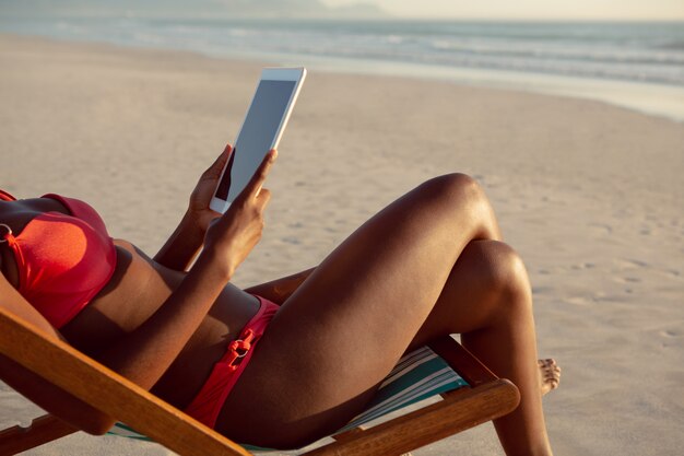 Donna che utilizza compressa digitale mentre rilassandosi in una sedia di spiaggia sulla spiaggia