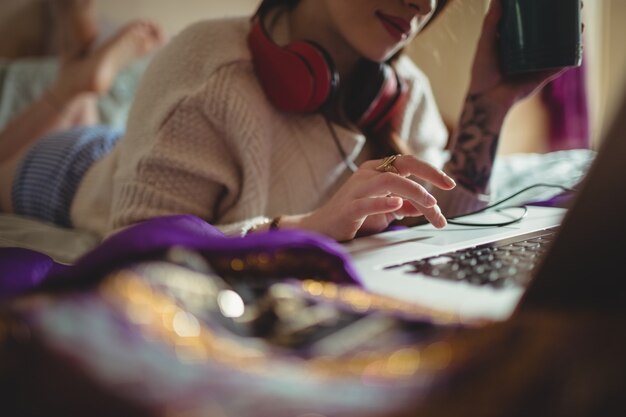 Donna che utilizza computer portatile mentre si prende il caffè sul letto