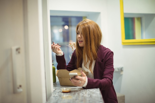 Donna che utilizza il telefono cellulare mentre si mangia insalata