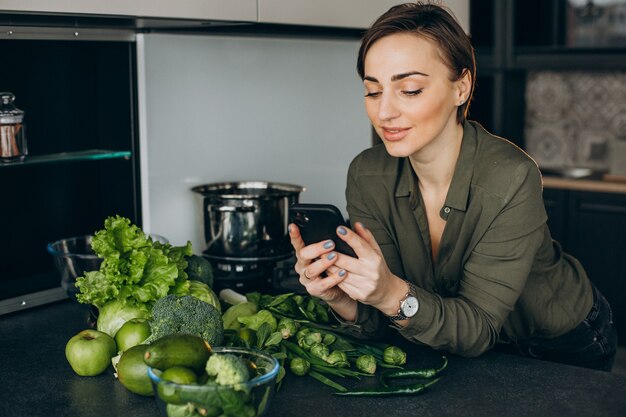 Donna che utilizza il telefono in cucina e cucinare il pasto di verdure verdi