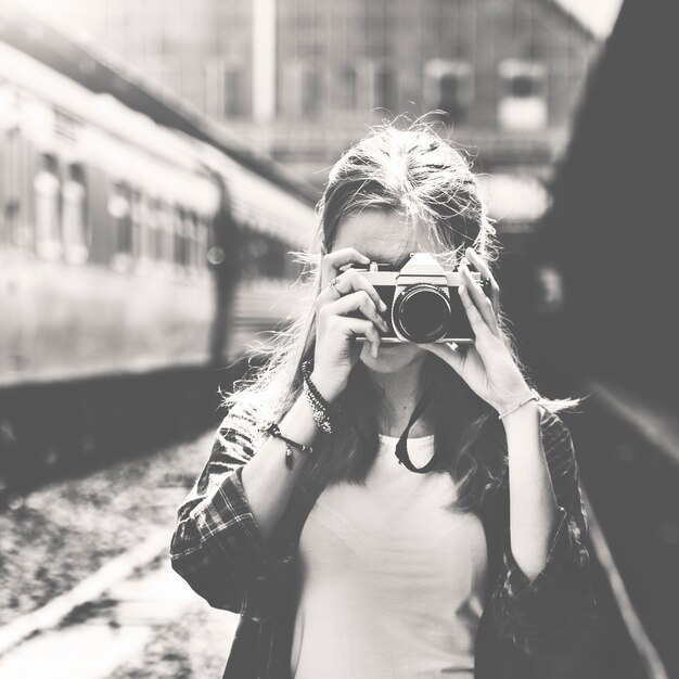 Donna che utilizza la fotocamera per scattare una foto alla stazione ferroviaria in scala di grigi