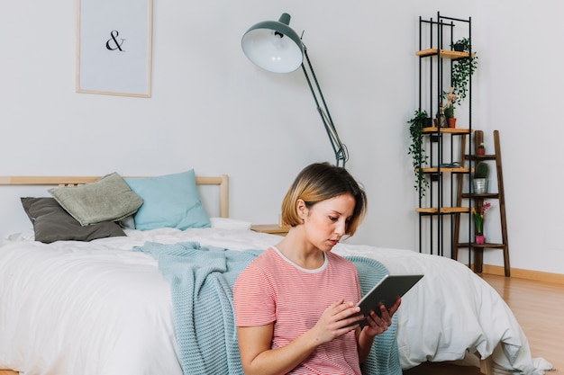 Donna che utilizza la tavoletta sul pavimento della camera da letto