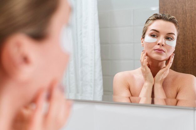 Donna che utilizza riducendo le toppe delle occhiaie nel bagno