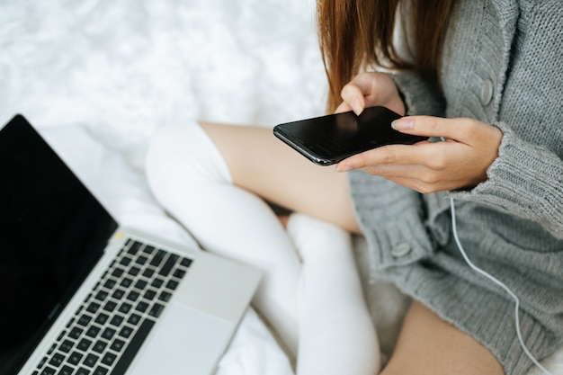 Donna che utilizza smartphone sul suo letto in una giornata fredda