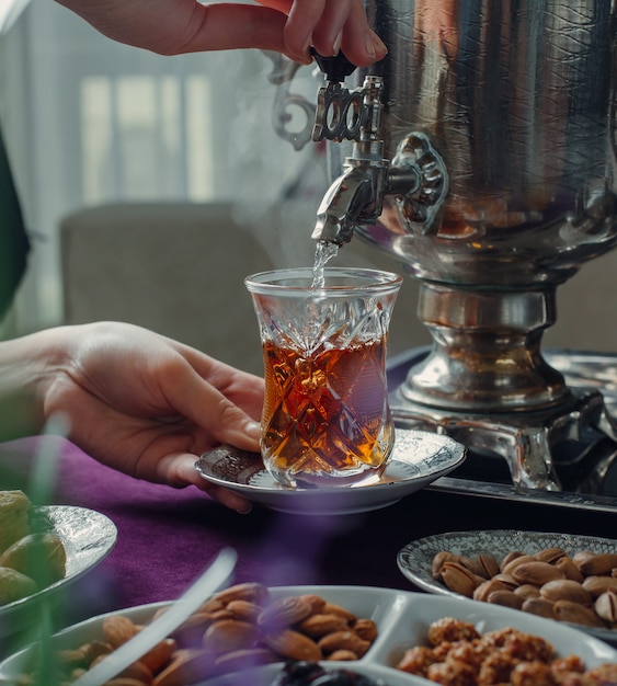 donna che versa acqua calda nel bicchiere con tè nero da samovar