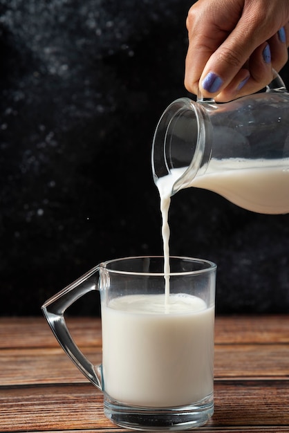 Donna che versa il latte nella tavola di legno della tazza di vetro.