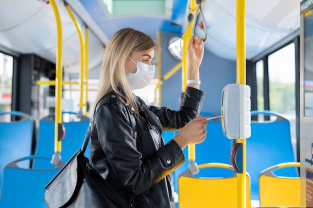 Donna che viaggia in autobus pubblico che indossa una maschera medica per protezione e usa il pass dell'autobus