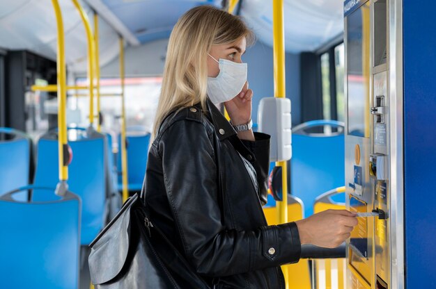 Donna che viaggia in autobus pubblico parla al telefono mentre indossa una maschera medica per protezione