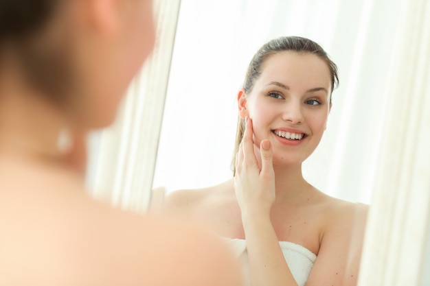 Donna con asciugamano sul corpo dopo la doccia, guardando nello specchio