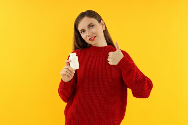 Donna con bottiglia di pillole su sfondo giallo