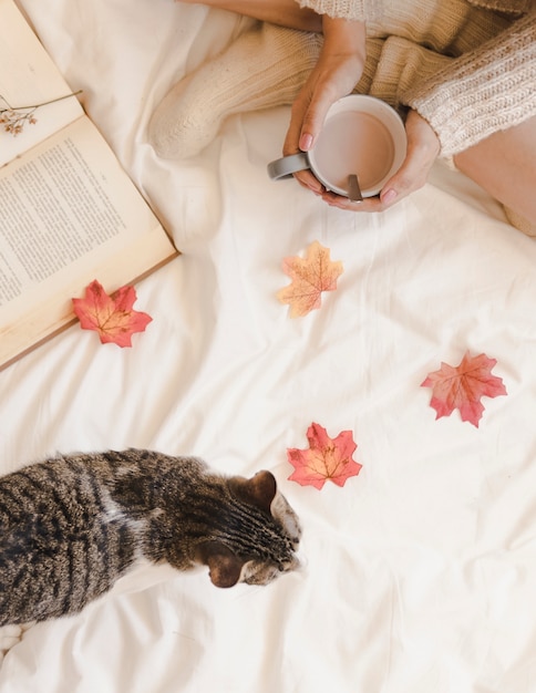 Donna con caffè vicino a gatto e libro