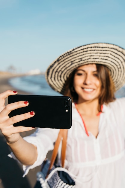Donna con cappello prendendo selfie in spiaggia