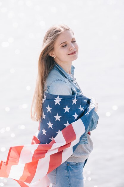 Donna con gli occhi chiusi in piedi avvolto in sventolando la bandiera americana