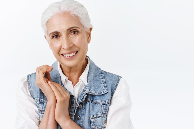 donna con i capelli grigi in elegante gilet di jeans, toccando le mani, applicando quotidianamente una crema anti-età, prendendosi cura di prodotti per la cosmetologia della pelle