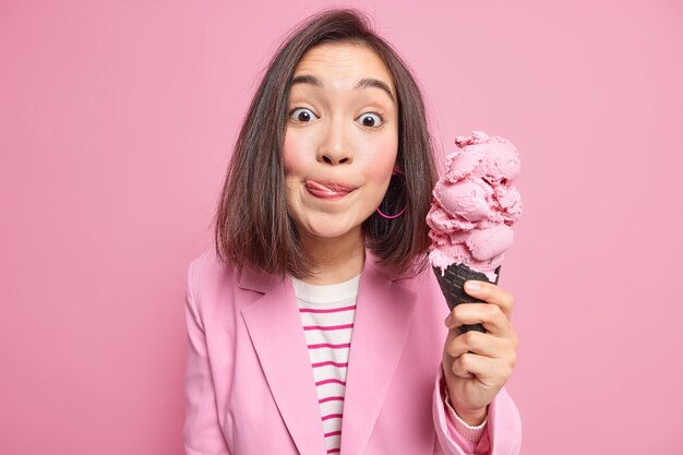 donna con i capelli scuri si lecca le labbra muore di fame per mangiare il gelato ama il dolce cibo spazzatura vestita in modo formale