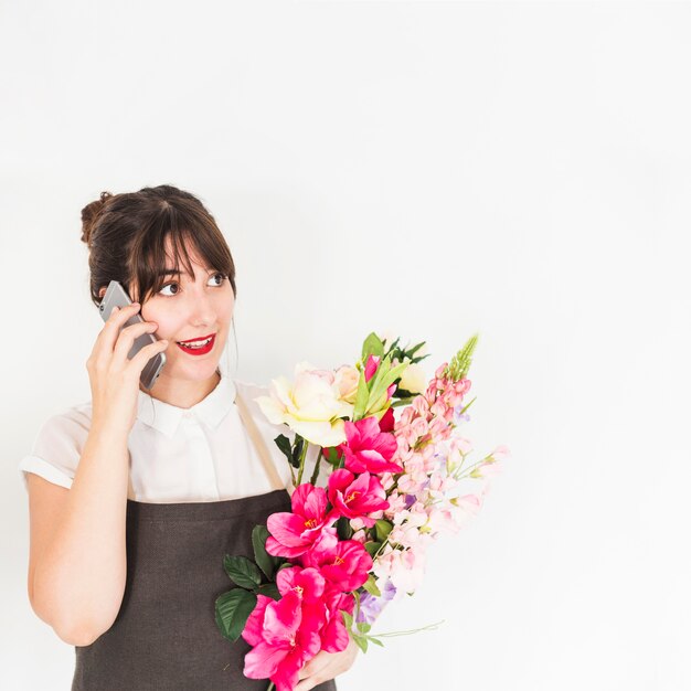 Donna con i fiori che parla sul cellulare contro fondo bianco