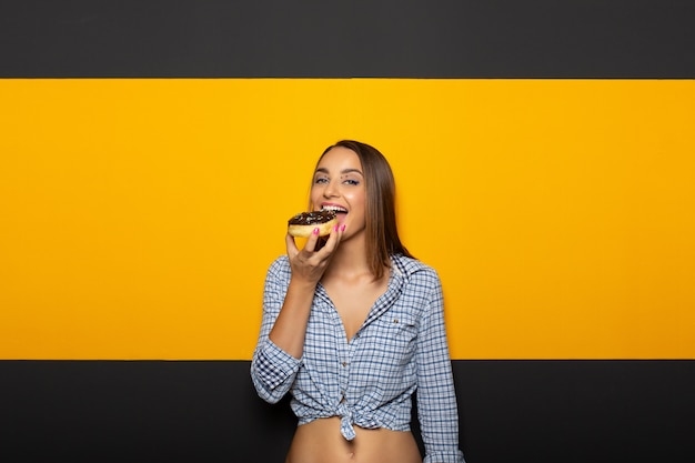 Donna con il sorriso luminoso bianco che mangia ciambella saporita.