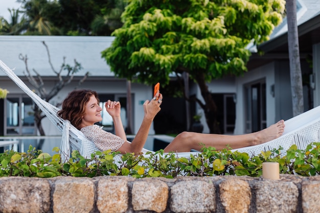 Donna con il telefono che riposa sdraiato sull'amaca con il telefono cellulare