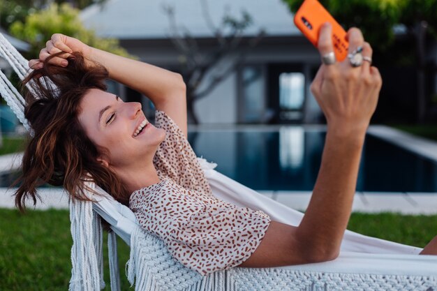 Donna con il telefono che riposa sdraiato sull'amaca con il telefono cellulare