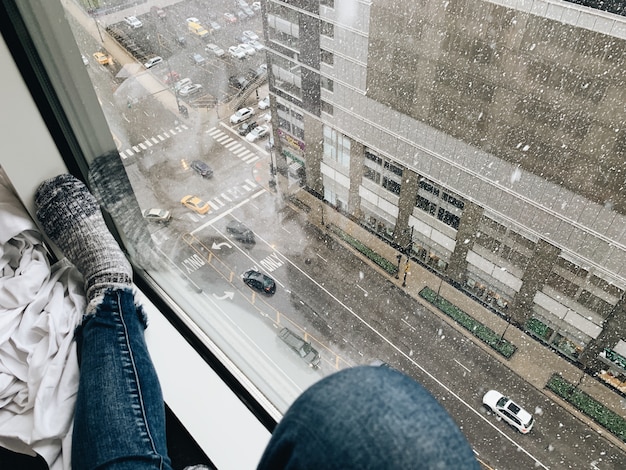 Donna con jeans e calze vicino a una finestra che guarda verso il basso per le strade