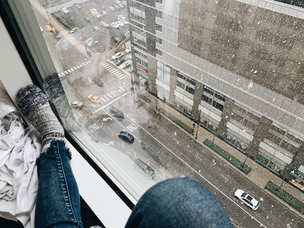 Donna con jeans e calze vicino a una finestra che guarda verso il basso per le strade