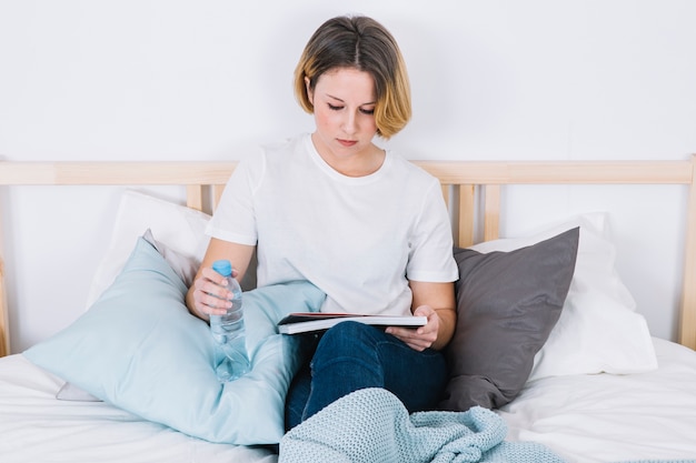 Donna con la lettura di bottiglia d&#39;acqua sul letto