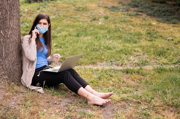 Donna con la mascherina medica che lavora al computer portatile all'aperto