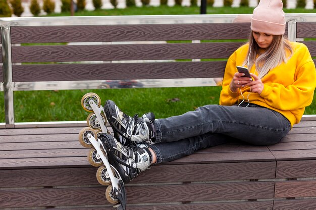 Donna con le lame del rullo che si siedono sul banco e che esaminano telefono