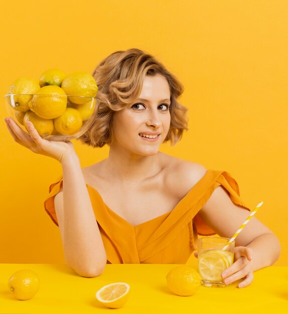 Donna con limonata e tenendo la ciotola con limoni