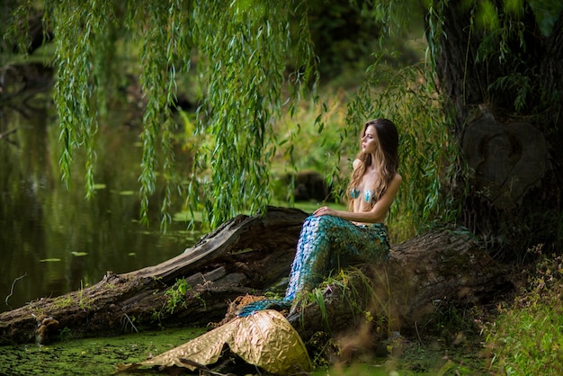 donna con lunghi capelli castani e vestita come una sirena siede sulla pietra sopra l'acqua