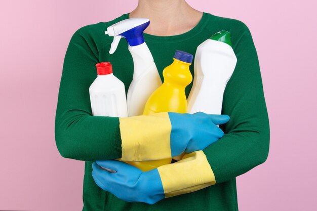 Donna con maglione verde che abbraccia molti prodotti per la pulizia tra le braccia