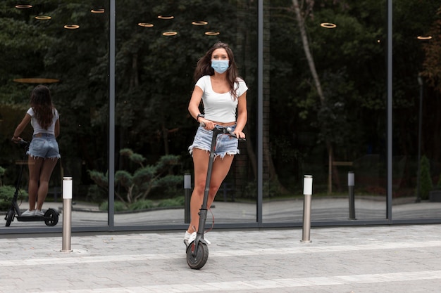 Donna con maschera in sella a uno scooter elettrico