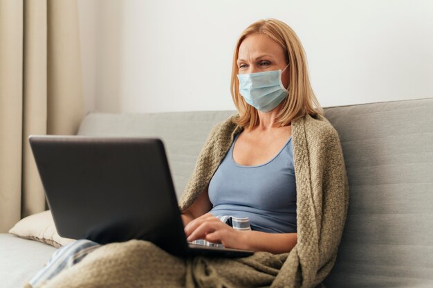 Donna con maschera medica che lavora al computer portatile a casa durante l'autoisolamento