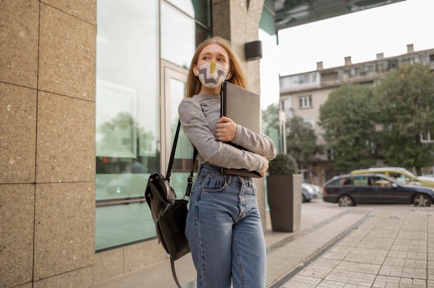 Donna con maschera medica che tiene il suo laptop all'esterno