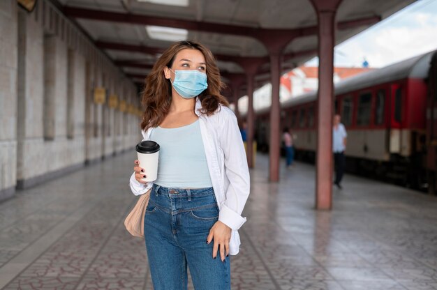 Donna con maschera medica e tazza di caffè alla stazione ferroviaria pubblica