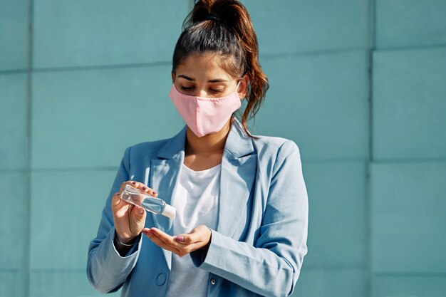 Donna con maschera medica in aeroporto utilizzando disinfettante per le mani durante la pandemia