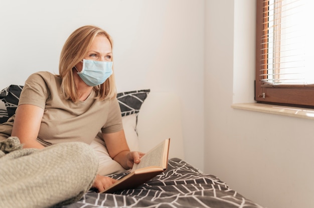 Donna con mascherina medica che legge in quarantena