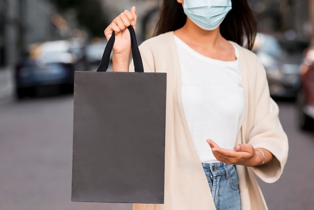 Donna con mascherina medica che mostra la borsa della spesa che sta tenendo