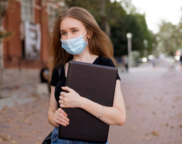 Donna con mascherina medica che tiene un computer portatile