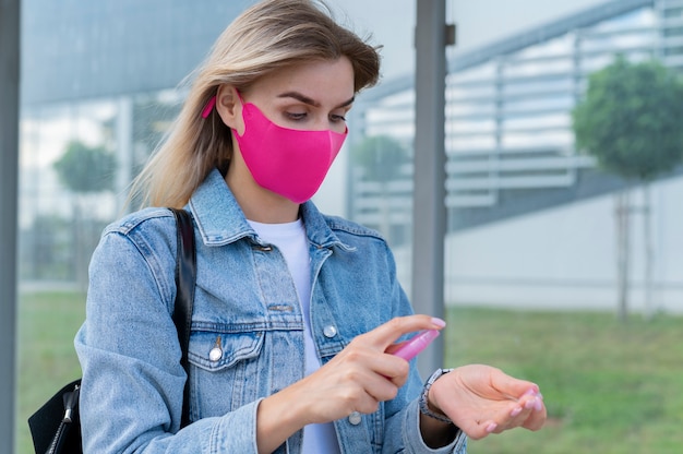 Donna con mascherina medica che usa disinfettante per le mani mentre aspetta l'autobus pubblico