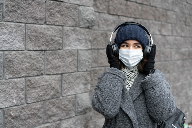 Donna con mascherina medica in città ascoltando musica in cuffia