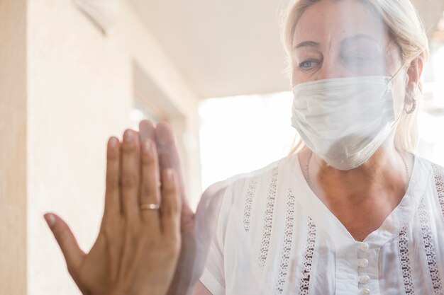 Donna con mascherina medica in quarantena dietro la finestra