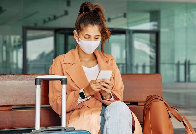 Donna con mascherina medica utilizza lo smartphone in aeroporto durante la pandemia