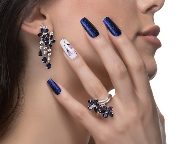 Donna con nail art che promuove design orecchini e anello di lusso.