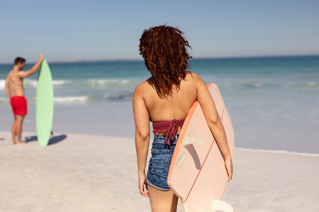 Donna con tavola da surf in piedi sulla spiaggia al sole