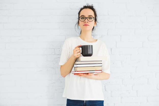 Donna con tazza e libri guardando la fotocamera