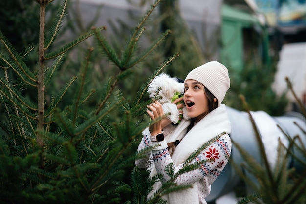 Donna con un cane bianco in braccio vicino a un verde alberi di Natale