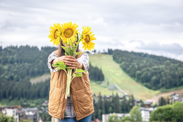 Donna con un mazzo di girasoli in natura in una zona montuosa