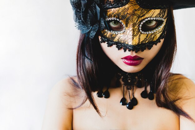 Donna con una maschera d&#39;oro veneziano e un cappello nero su sfondo bianco