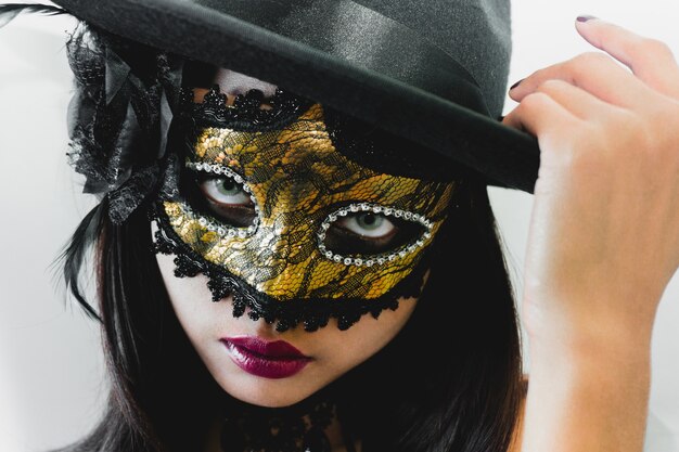 Donna con una maschera d'oro veneziano e un cappello nero su sfondo bianco
